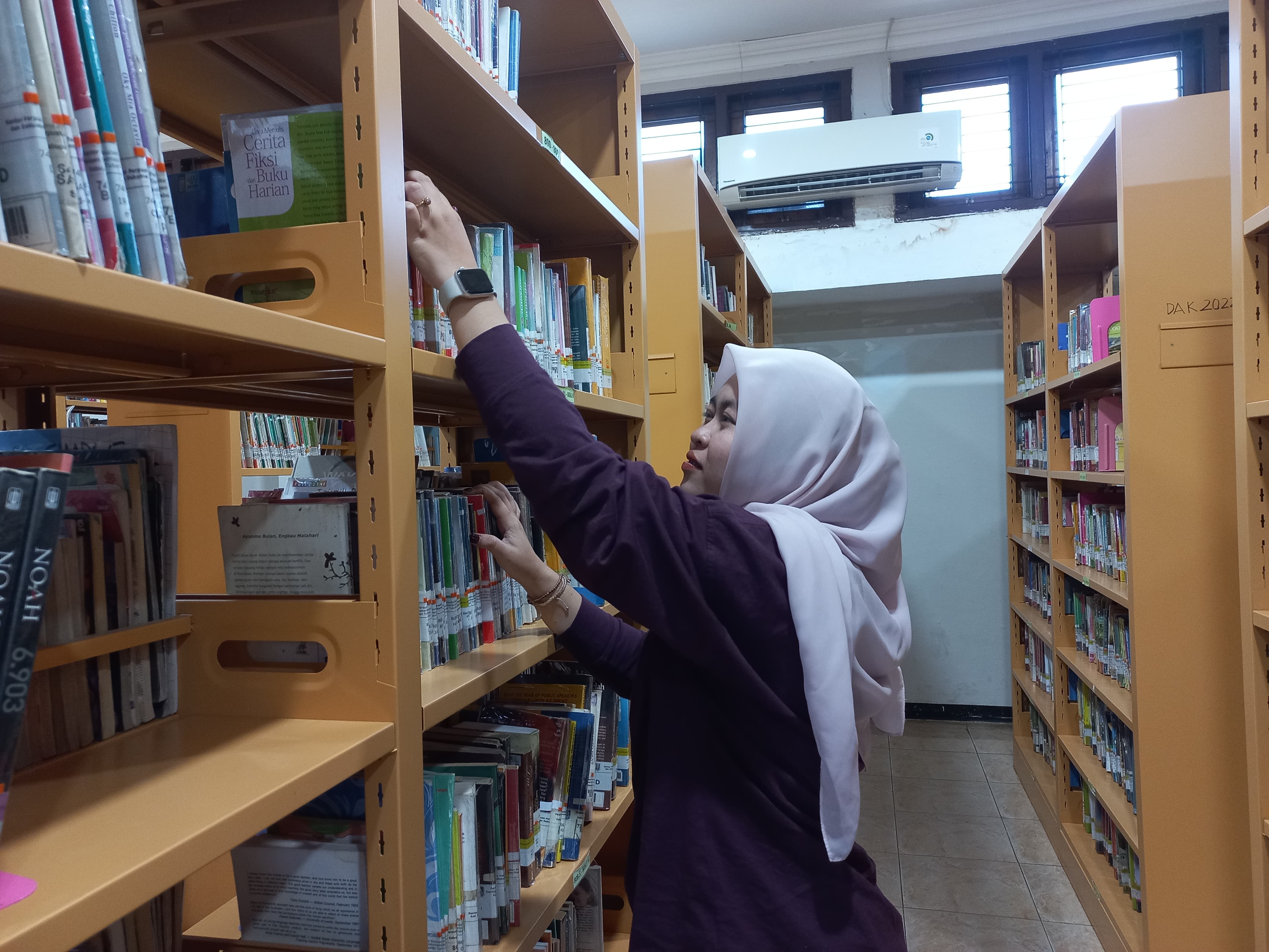 Salah seorang pengunjung perpustakaan tengah mengambil salah satu buku yang ingin dibacanya.
