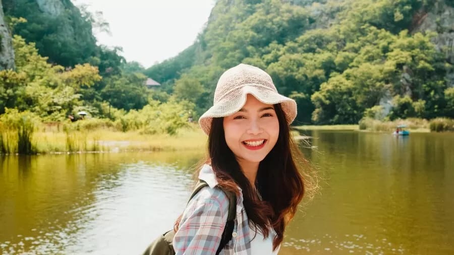 Seorang wanita tersenyum dengan latar belakang pemandangan indah, menggambarkan kebebasan dan kegembiraan perjalanan solo yang aman.
