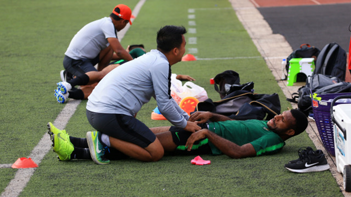 Ilustrasi seorang fisioterapis tengah menangani pemain sepak bola yang mengalami keluhan di lapangan.