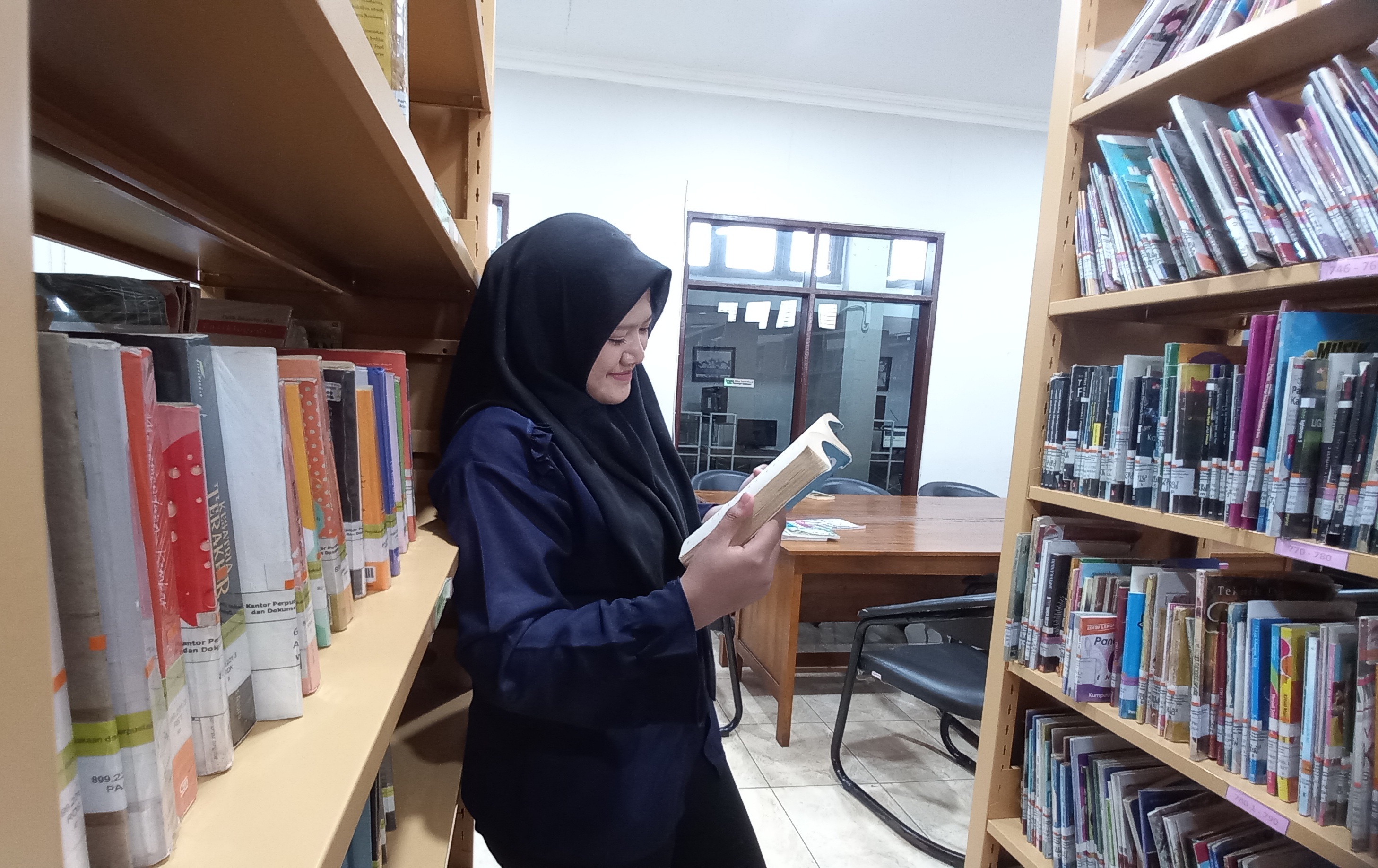 Salah seorang pengunjung Perpusda tengah asyik membaca novel di antara rak-rak buku kesusastraan.