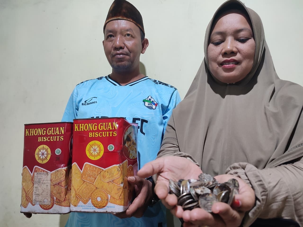 Mohammad Nasrudin ditemani istrinya, Hariyati menunjukkan kaleng biskuit dan koin karatan yang sebelumnya ditabung selama sebelas tahun.