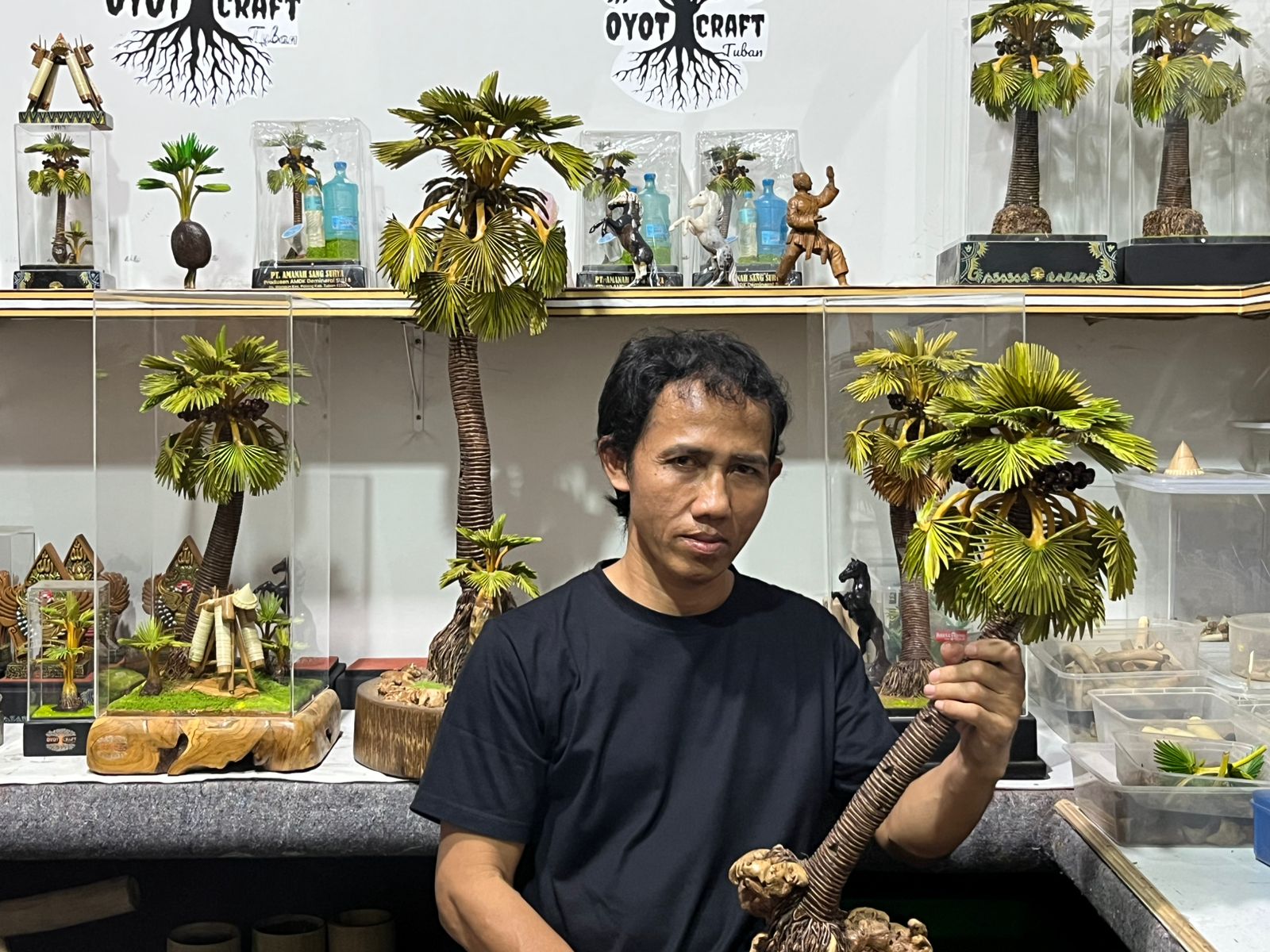 Putra Hadi Mulyo berfoto bersama karya miniatur pohon siwalan di bengkel kerajinan rumahnya, Desa Tegalagung, Kecamatan Semanding.