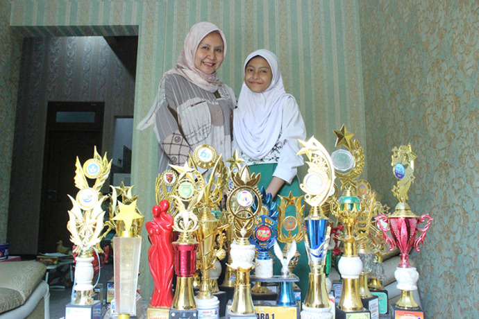 KECIL CABE RAWIT: Madeleine Soraya Andya dipeluk Rizka Nahdiyah Soraya, ibunya. Di depannya berjejer piala berbagai kejuaraan. (Yudha Satria Aditama/Radar Tuban)