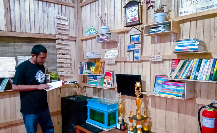 NYAMAN: Kepala Desa Guyangan Hasyim membaca salah satu buku di pendapa rest area.