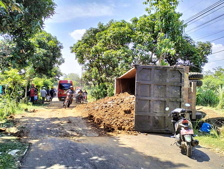 TERGULING: Sebuah truk tronton bermuatan tanah uruk proyek Tol Probowangi terguling setelah menabrak dua motor di jalan Desa Condong, Kecamatan Gading, Kabupaten Probolinggo. (Achmad Arianto/Jawa Pos
