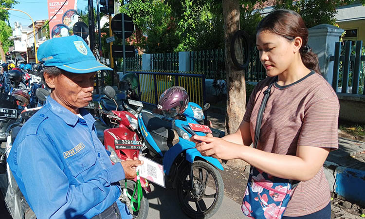 NONTUNAI: Seorang pemilik kendaraan bermotor membayar retribusi parkir dengan cara nontunai pada juru parkir di Pasar Baru Kota Probolinggo.