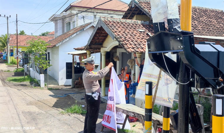 PASANG: Petugas kepolisian saat memasang banner peringatan di perlintasan sebidang.
