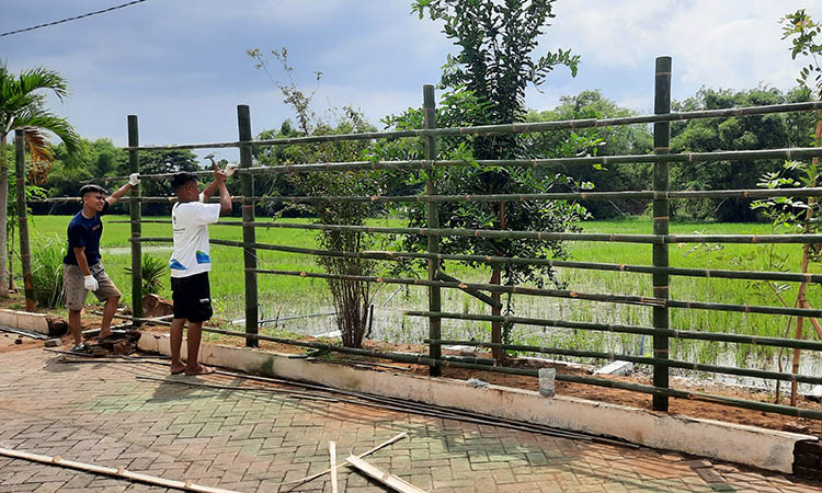 SEMENTARA: Pekerja membuat pagar bambu sementara untuk mengganti pagar tembok belakang gudang farmasi yang roboh.