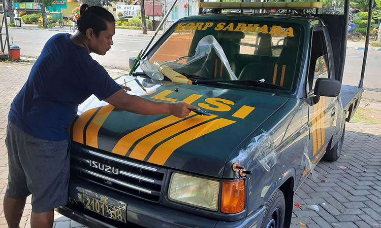MEMASANG: Irul menempelkan stiker sesuai kebutuhan kendaraan dinas kepolisian.