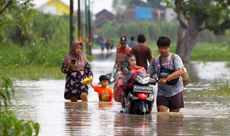 MENGUNGSI: Warga Kedungringin dengan motornya melintas di jalan utama permukiman desa setempat yang terendam banjir, Selasa (6/2) siang. Banjir setinggi satu meteran membuat dusun tersebut terisolir.