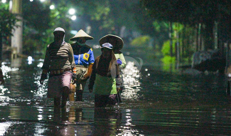 GANGGU AKTIVITAS: Warga Kedungringin berjalan di jalan yang tergenang air setinggi lutut.