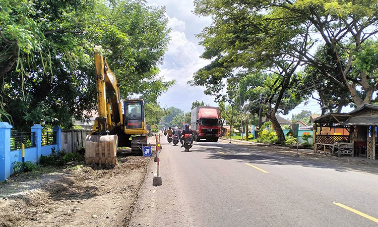 DILEBARKAN: Pekerja mengeruk bahu jalan Jalur Pantura Kecamatan Paiton, menggunakan ekskavator.&nbsp;
