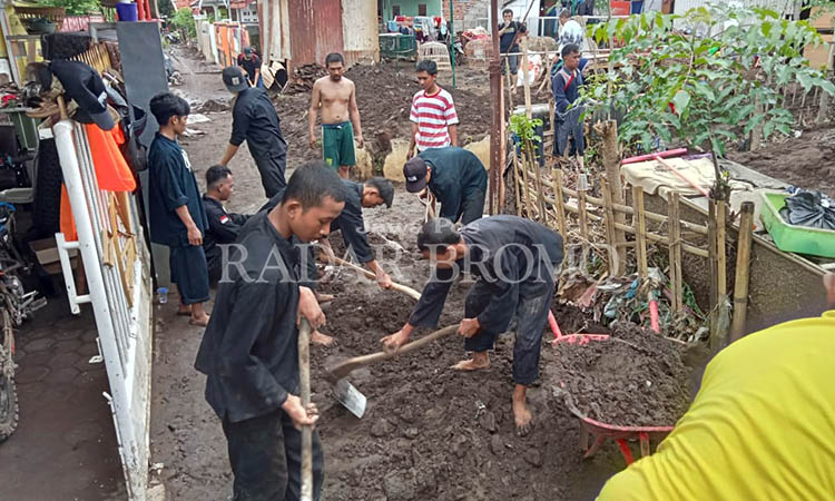 BANTU WARGA: Sukarelawan dari semua cabor di KONI Kabupaten Probolinggo membantu warga Kedungdalem dan Dringu, membersihkan material lumpur sisa banjir yang menumpuk di dala