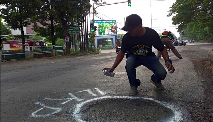 TANDAI YANG BAHAYA: Relawan Info Lalu Lintas dan Kriminal (ILK) Pasuruan menandai jalanan yang berlubang dan bergelombang dengan cat Pilox putih di sepanjang jalan kawasan Raci-Kraton. (M Busthomi)