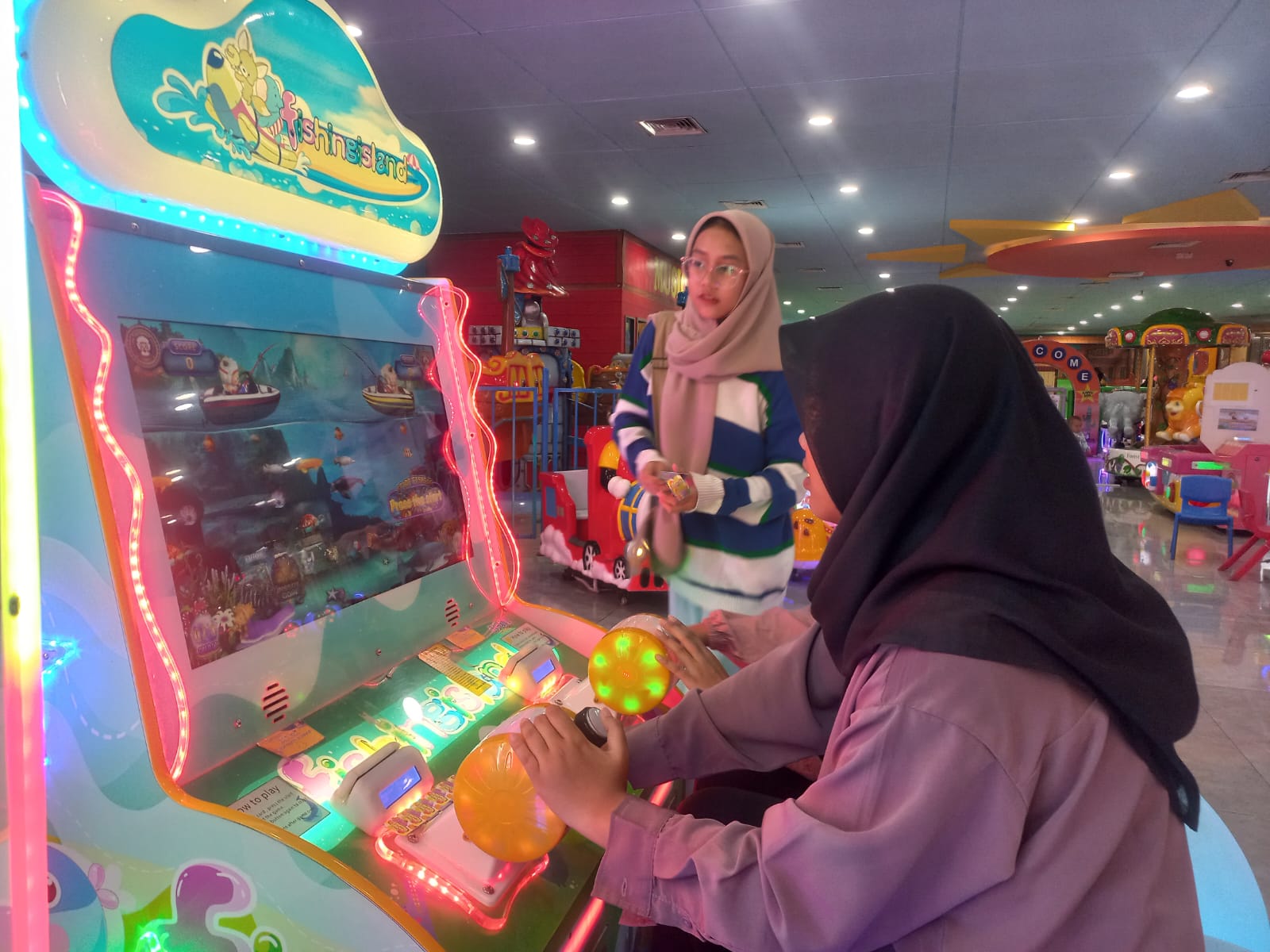 FOKUS: Nadhisa Ayu Listi Abdulla (kerudung hitam) dan Nazhima Zahra Shafira Putri (kerudung coklat) saat bermain game Fishing Island.