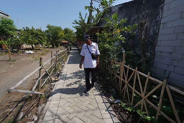 LEBIH BAIK: Salah satu perangkat Desa Asembagus, Kecamatan Kraksaan, melintas di jalan Dusun Calokelang, yang telah rampung dipaving.