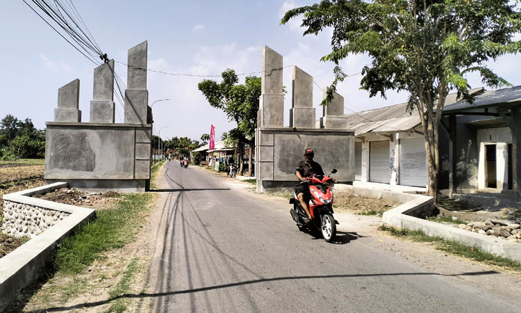 TERITORIAL: Warga melintas di gapura desa di RT 2/RW 5, Dusun Bedien. Wilayah ini nantinya akan dibangun secara bertahap.