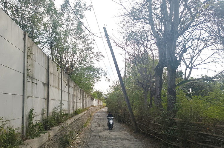 MIRING: Seorang pengendara motor melintas di jalan dekat tiang listrik PLN di Desa Tigasan Wetan, Kecamatan Leces, Kabupaten Probolinggo, yang miring.