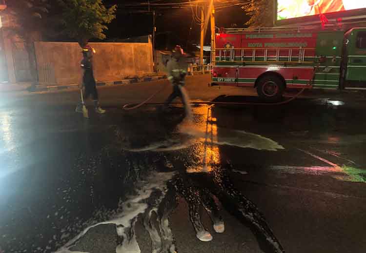 SEMPROT: Tim Damkar Satpol PP Kota Probolinggo membersihkan tumpahan oli di tikungan Jalan Pahlawan menuju Perempatan Brak, Kota Probolinggo, Selasa (24/9) malam.