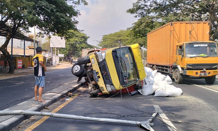 TERGULING: Truk muatan beras yang terguling di Legok, Kecamatan Gempol usai mengalami pecah ban dan menabrak tiang PJU di tengah median jalan.