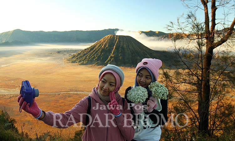 EKSOTIS: Dua wisatawan berpose dengan background Gunung Batok dan Bromo. Tarif tiket masuk wilayah Gunung Bromo alami kenaikan mulai 30 Oktober. (Mokhamad Zubaidillah/ Radar Bromo)