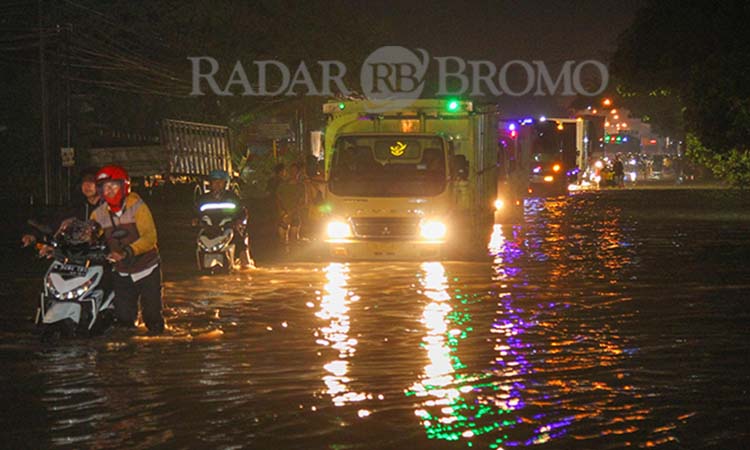 JADI SUNGAI DADAKAN: Salah satu pengendara motor menuntun motornya melewati ruas pantura Kraton, Kabupaten Pasuruan yang terendam banjir. (Mokhamad Zubaidillah/ Radar Bromo)