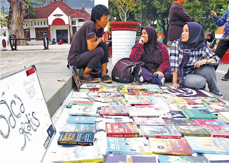 GRATIS: Dua pengunjung berkomunikasi dengan salah seorang pegiat literasi jalanan yang menyediakan buku bacaan di Taman Kota, Kota Pasuruan.