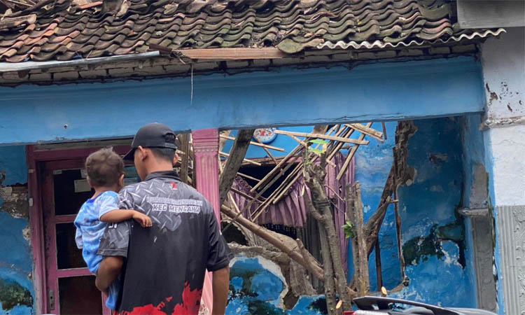 TAK LAYAK HUNI: Syafiudin menggendong Raka, putranya di depan rumahnya di Desa Sambirejo, Rejoso. Rumah Syafiudin tiba-tiba ambruk, Senin (17/12).