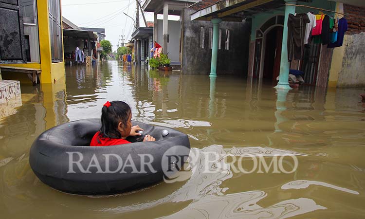 Seorang bocah main ban di tengah banjir yang menggenangi pemukiman padat penduduk di Beji, Kamis (16/1). (Mokhamad Zubaidillah/ Radar Bromo)