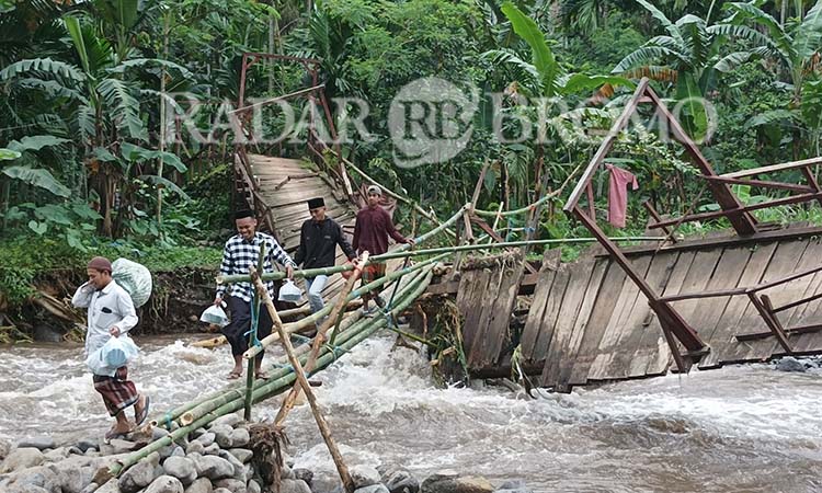 Sejumlah warga melintas melewati jembatan darurat dari bambu yang berdiri di atas jembatan yang terputus di Betektaman, Gading, Probolinggo. (Agus Faiz Musleh/ Radar Bromo)