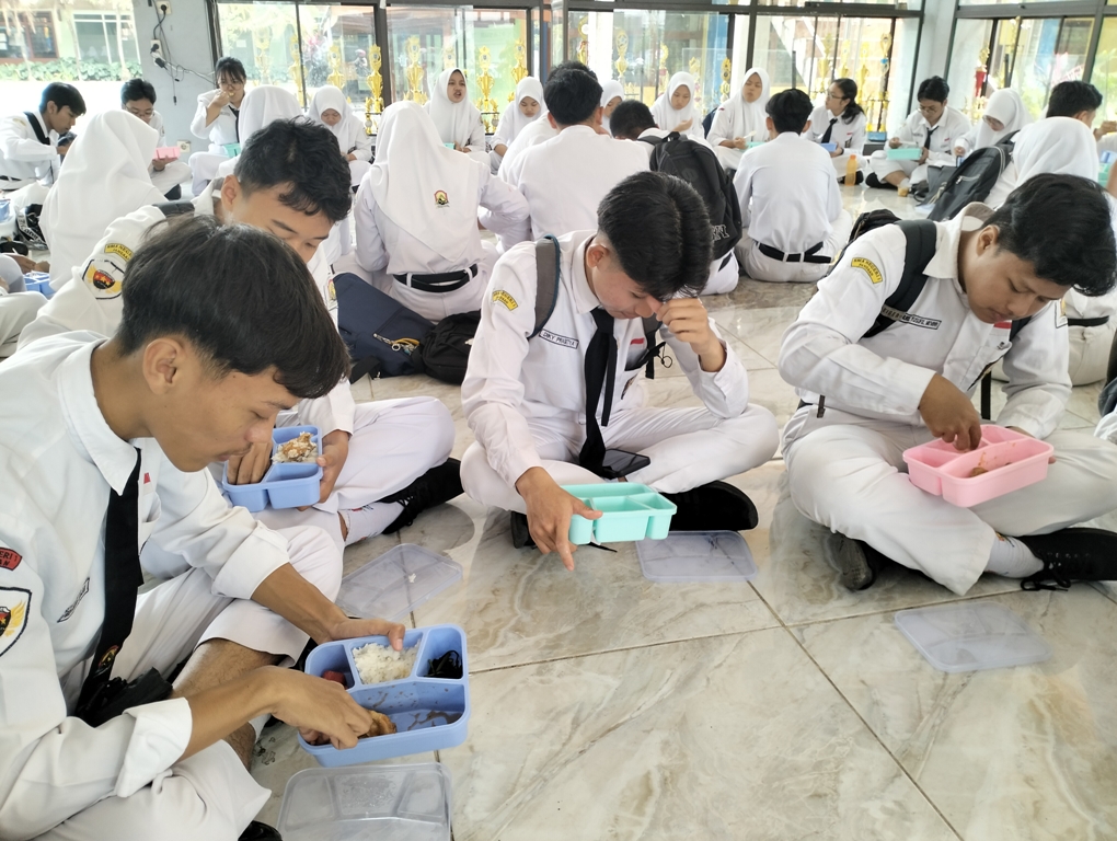 Para pelajar di SMAN 1 Pandaan menikmati menu MBG dengan memakai tangan dan duduk lesehan.
