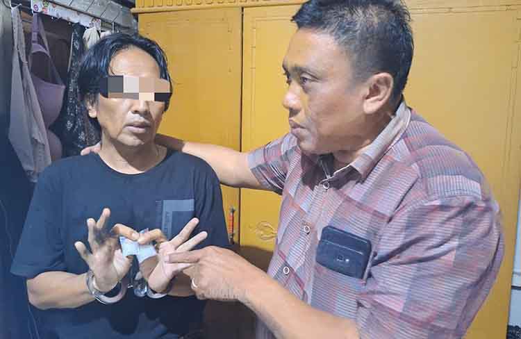 DIBEKUK: Haji Umar memegang barang bukti dua paket sabu yang ditemukan di rumahnya. Kini, ia ditahan di Mapolres Probolinggo.