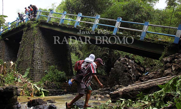 SAYANG ANAK: Seorang warga menggendong anaknya yang mau berangkat sekolah melintasi sungai usai jembatan Karangjati Anyar, Wonorejo Pasuruan ambrol, (13/5).