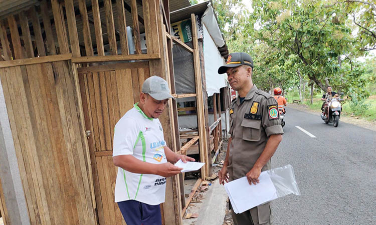 DIIMBAU: Petugas Satpol PP Kota Pasuruan saat memberikan imbauan kepada pedagang di Senani. Imbauan itu ditempel di warung pedagang, bagi mereka yang tak ada di lokasi.