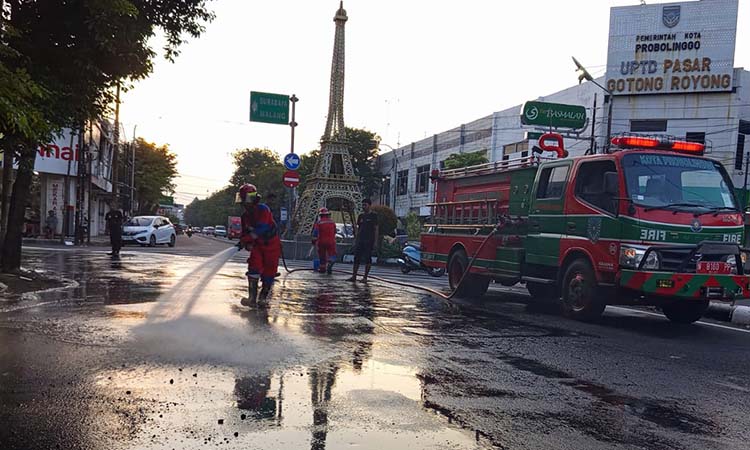 DISEMPROT: Petugas Damkar Satpol PP Kota Probolinggo saat membersihkan tumpahan solar di tikungan Menara Eiffel Kota Probolinggo (30/5).