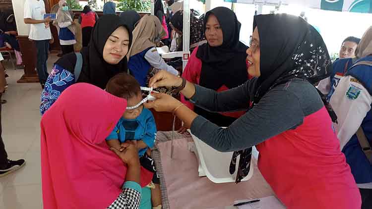 PENGUKURAN: Petugas kesehatan mengukur lingkar kepala salah seorang balita.