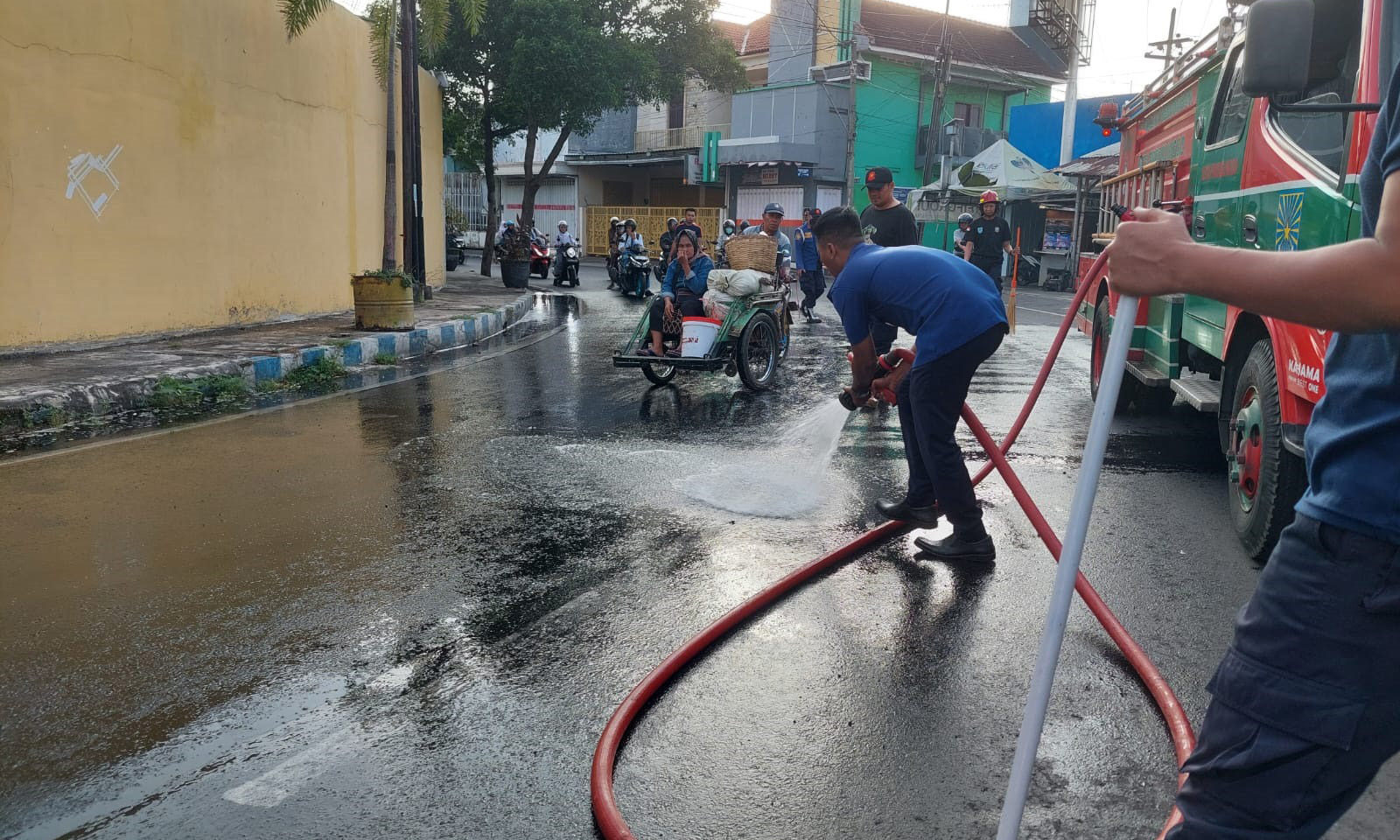 SEMPROT: Tim Damkar Satpol PP Kota Probolinggo membersihkan tumpahan solar di Jalan Pahlawan, Kota Probolinggo, Senin (14/7) pagi.
