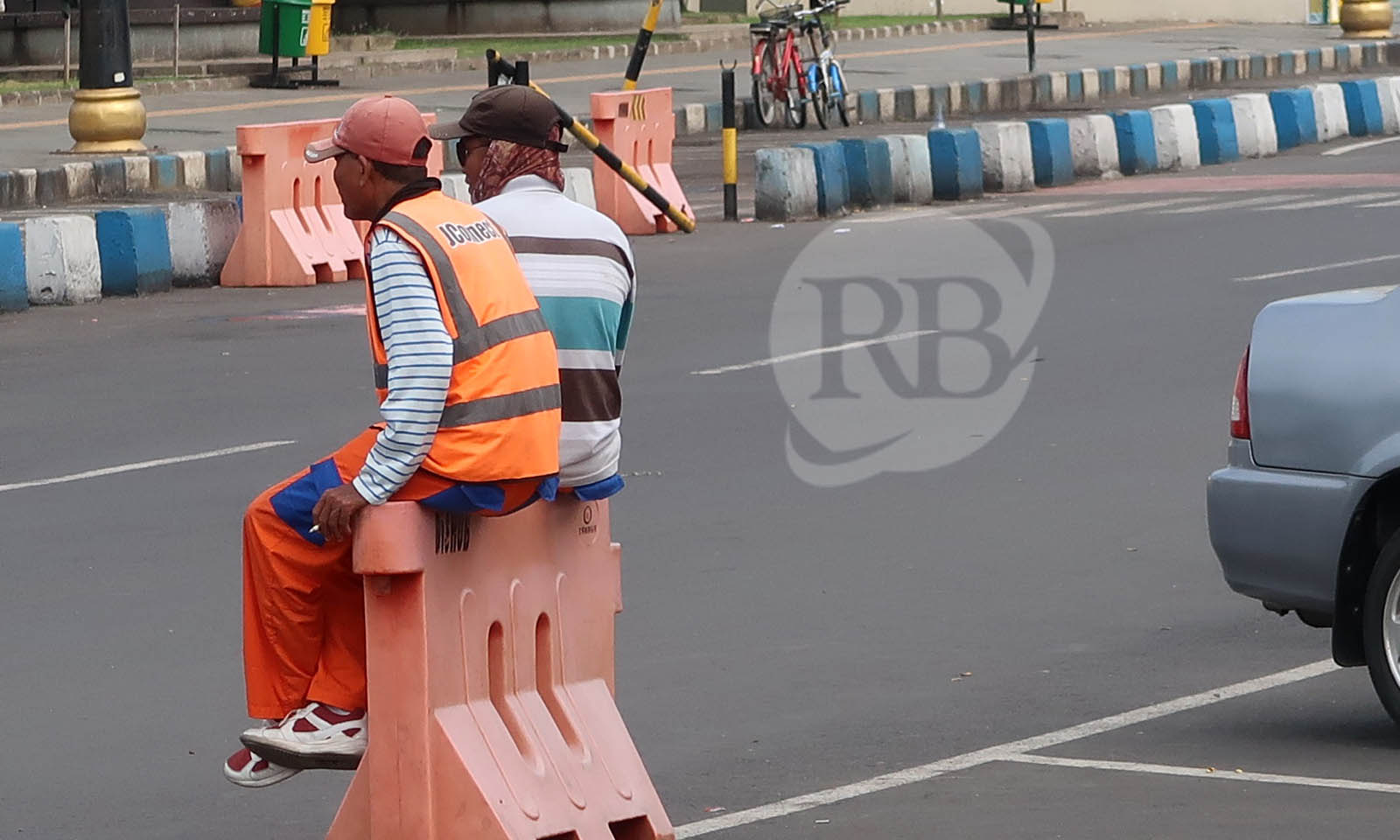 TERGANTUNG KONDISI: Juru parkir duduk di atas water barrier di kawasan Alun-alun Pasuruan sembari menunggu kendaraan parkir.
