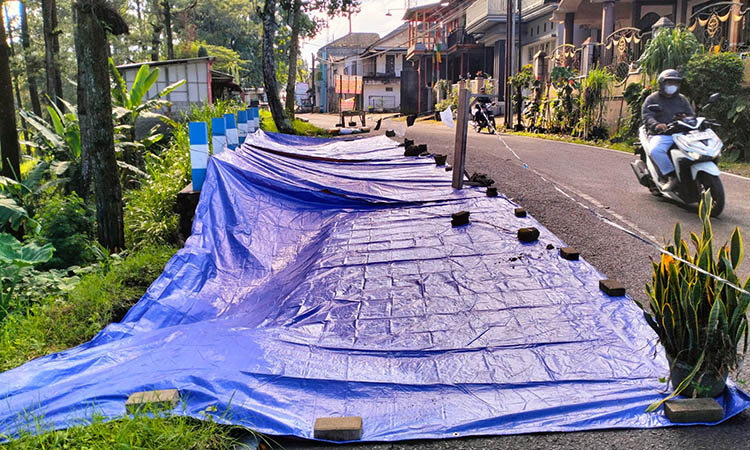 BIAR AMAN: Pemasangan terpal di bahu jalan yang ambles. Hal ini dilakukan, sebagai penanda agar pengguna jalan lebih waspada.
