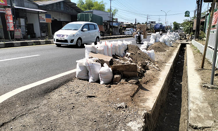 DITINGGAL: Tumpukan tanah sedimentasi hasil kerukan saluran air yang dibiarkan begitu saja oleh pekerja. Kondisi itu dikeluhkan, lantaran dianggap membahayakan. Serta, mengganggu pelaku usaha.