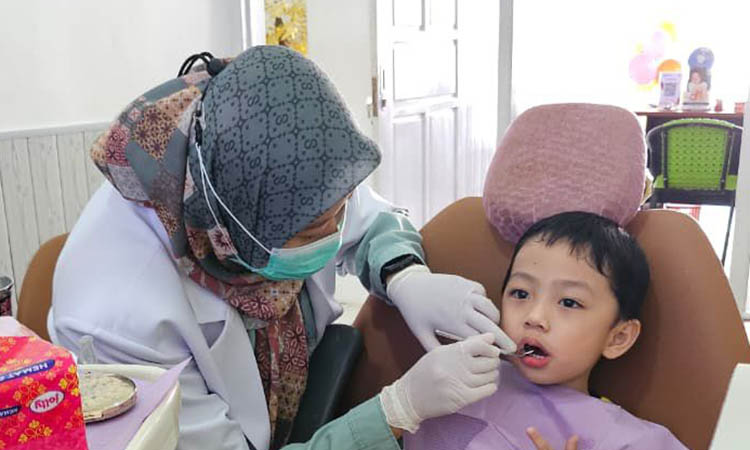 PEMERIKSAAN: drg. Andina Muzayyanti memeriksa kondisi gigi pasien anak kecil. Pemeriksaan ini penting dilakukan untuk menjaga gigi tetap sehat.