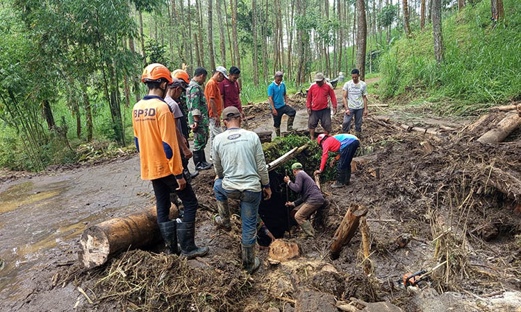 BERSIHKAN: Gabungan personel BPBD Kabupaten Pasuruan, Perhutani dan warga saat bahu membahu membersihkan material longsor.