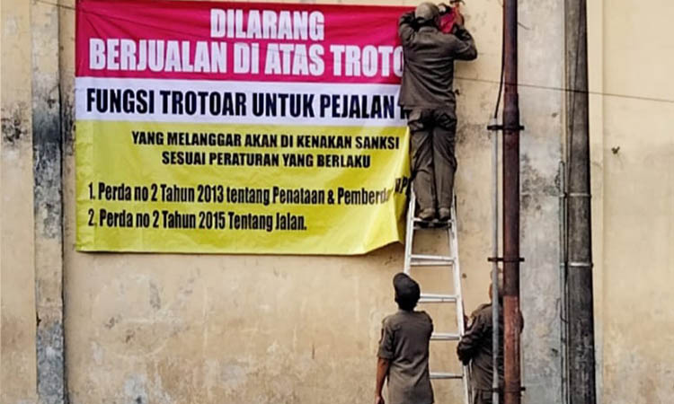 HARUS SABAR: Personel Satpol PP memasang banner imbauan larangan berjualan di sisi Barat depan Stasiun Pasuruan.