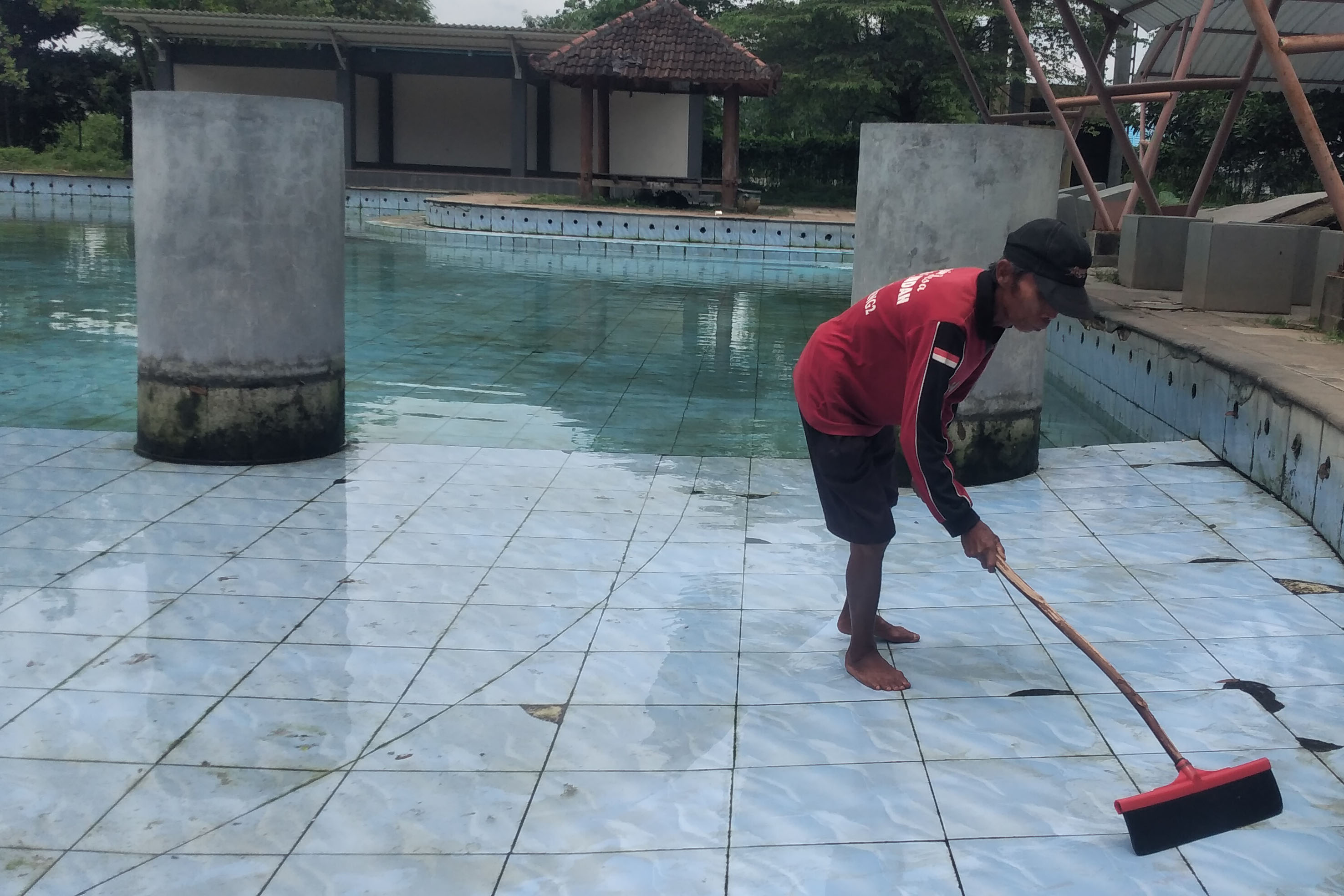 BERTAHAN: M. Sueb, seorang PKL yang bertahan di Umbulan Park, membersihkan kolam dengan harapan ada pengunjung dan membeli dagangannya.