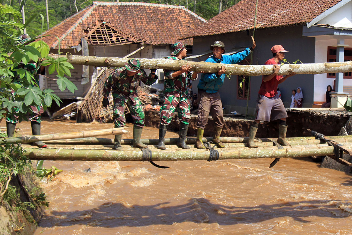 DAMPAK BENCANA: Anggota TNI dibantu warga saat membangun jembatan darurat untuk menggantikan jembatan yang terbawa banjir bandang, beberapa waktu lalu.
