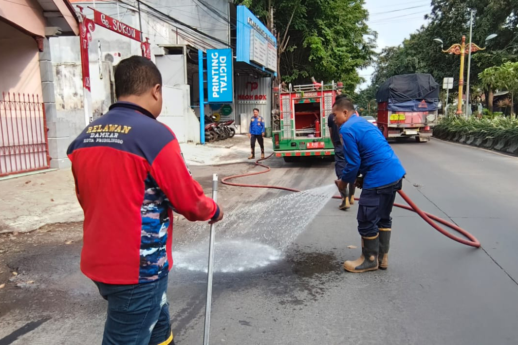 SIRAM: Tim Damkar Satpol PP Kota Probolinggo menyemprot tumpahan oli di Jalan Panglima Sudirman, Kota Probolinggo, Jumat (6/2).