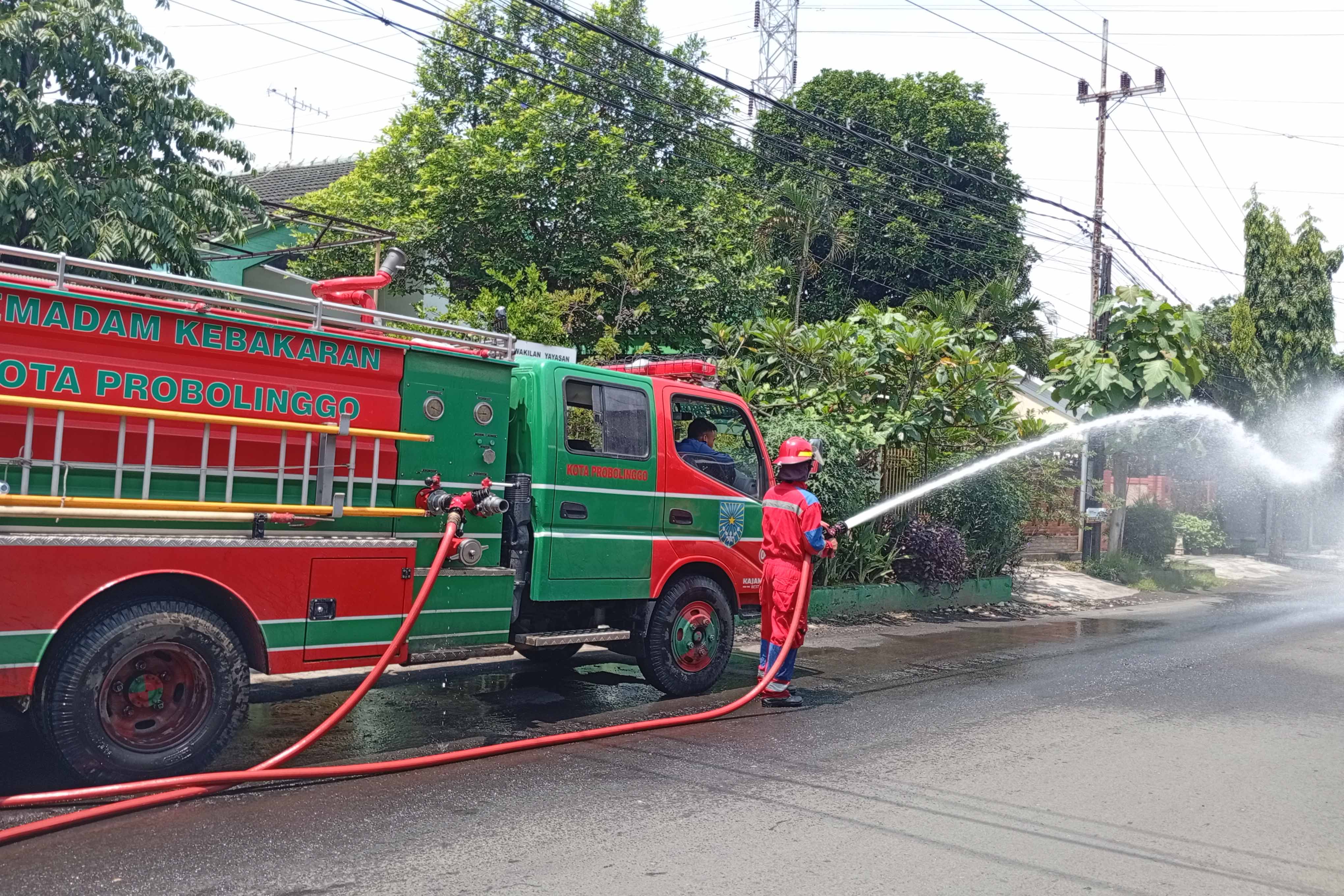 DIBERSIHKAN: Tim Damkar Satpol PP Kota Probolinggo membersihkan ceceran oli di Jalan Slamet Riyadi, Kota Probolinggo, Senin (9/2) pagi.
