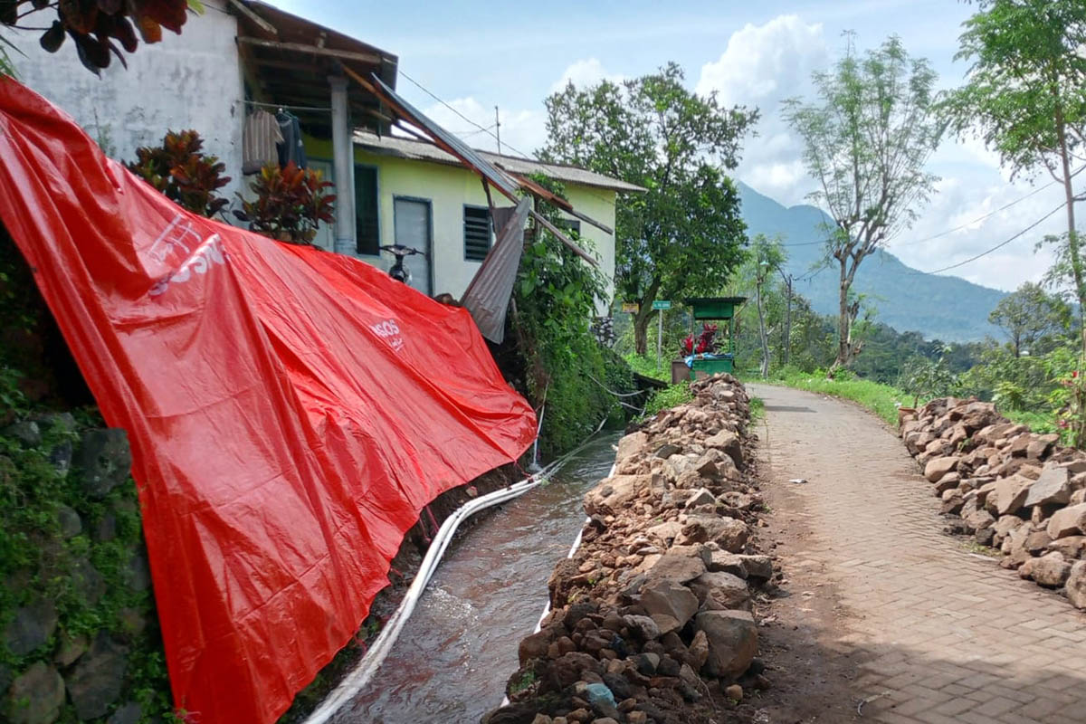 DITUTUPI: Plengsengan ambrol di Dusun Jagil, Desa Gambiran, Kecamatan Prigen yang ditutupi terpal. Hal itu dilakukan, agar kerusakannya tidak semakin parah.