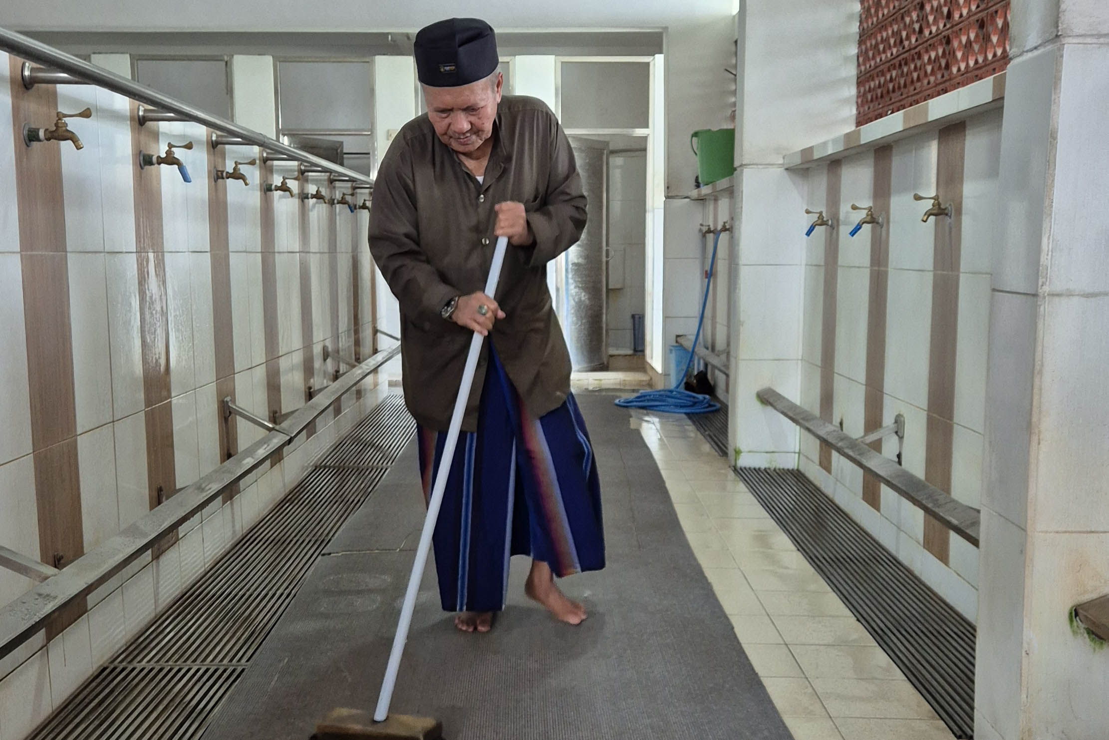 SEMANGAT MENGABDI: M. Suyono membersihkan areal tempat wudu dan kamar mandi laki-laki di Masjid Agung Al Anwar, Kota Pasuruan.