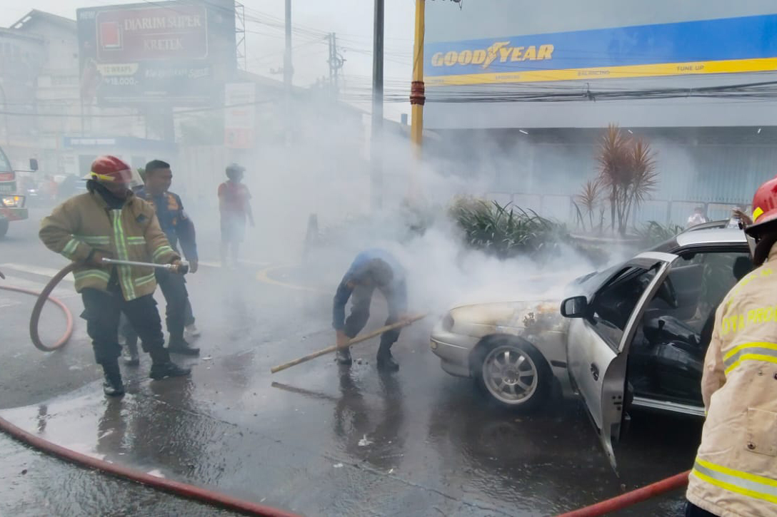 SEMPROT: Petugas Damkar Satpol PP Kota Probolinggo memadamkan api yang melalap Sedan Timor di Simpang Empat Randupangger, Kota Probolinggo, Minggu (22/2).